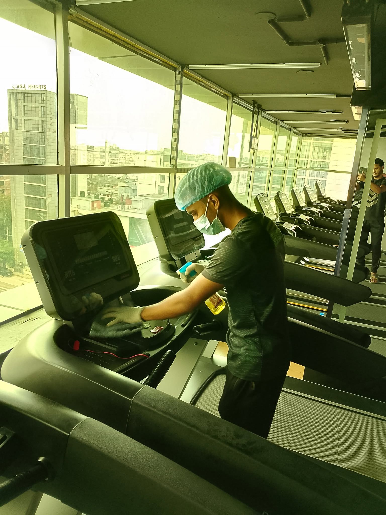 Staff member in mask and gloves sanitising a treadmill console